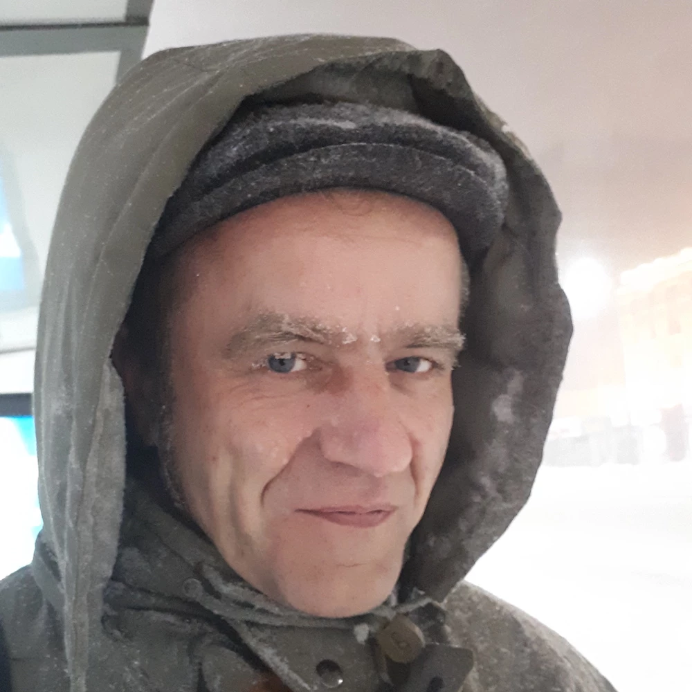 Person mit Kapuze lächelt in die Kamera, Schneeflocken im Gesicht, unscharfer Hintergrund mit Schneefall.